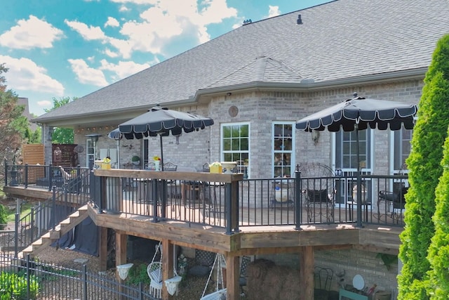 rear view of property featuring a deck, stairs, a shingled roof, brick siding, and outdoor dining space