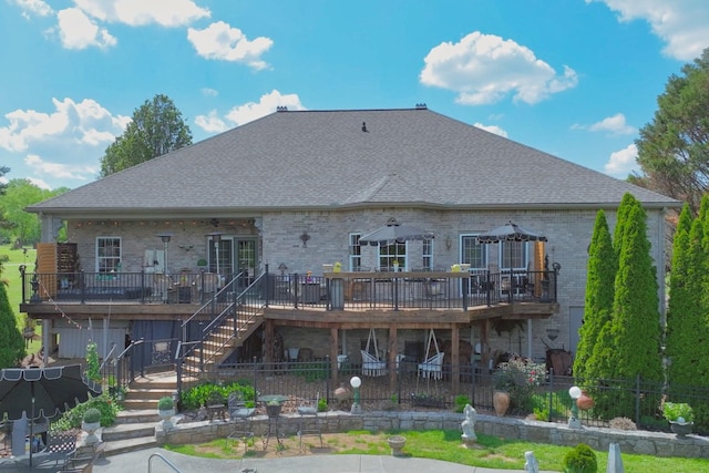rear view of property featuring brick siding, a wooden deck, stairs, and roof with shingles