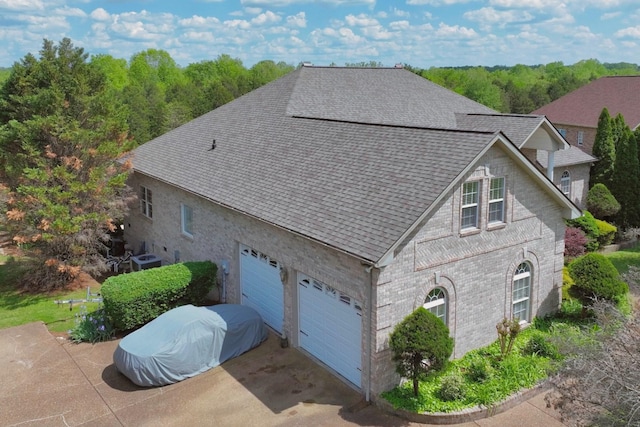 view of side of property with a shingled roof, cooling unit, driveway, and brick siding