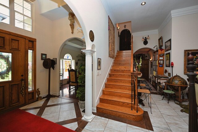 foyer featuring arched walkways, ornamental molding, a healthy amount of sunlight, and stairway