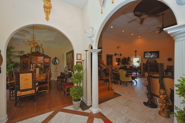 foyer entrance featuring arched walkways, ceiling fan with notable chandelier, ornate columns, a tray ceiling, and ornamental molding