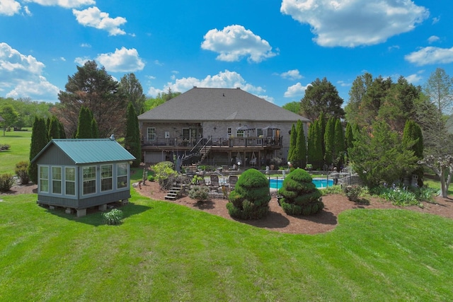 back of property with a lawn, a wooden deck, stairs, and an outdoor pool