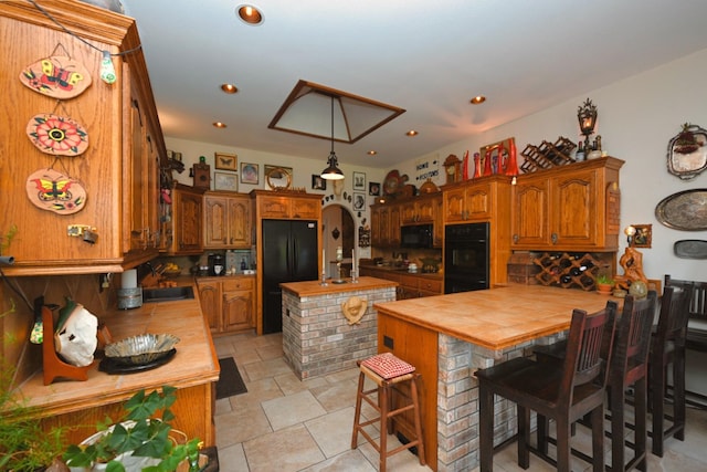 kitchen featuring butcher block countertops, an island with sink, brown cabinetry, tasteful backsplash, and black appliances