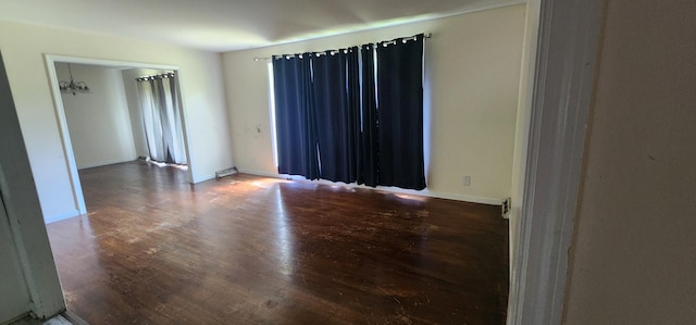 empty room featuring baseboards, wood finished floors, and a notable chandelier