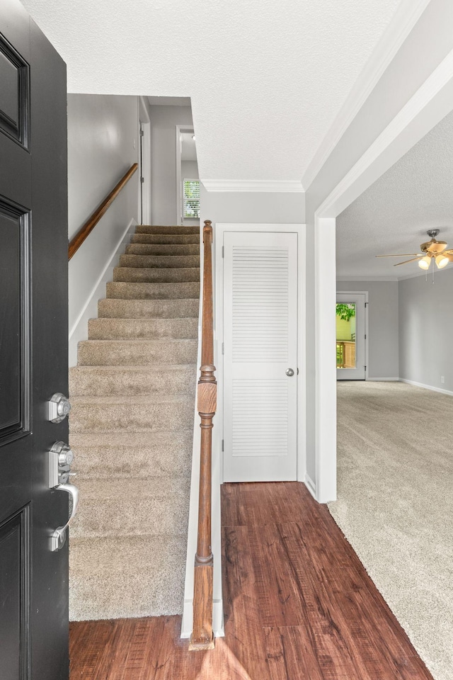 staircase featuring crown molding, baseboards, a ceiling fan, and a textured ceiling