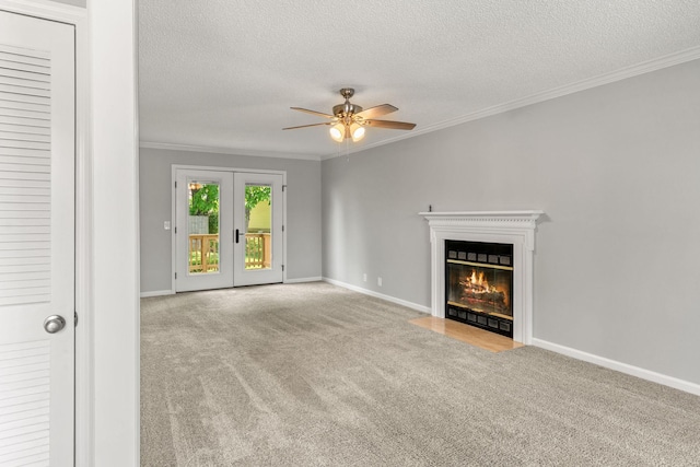 unfurnished living room featuring ceiling fan, french doors, crown molding, a fireplace with flush hearth, and carpet flooring