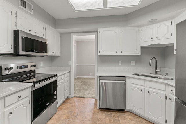 kitchen with white cabinets, appliances with stainless steel finishes, a sink, light countertops, and visible vents