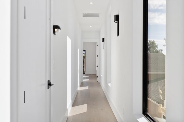 corridor featuring baseboards, light wood-type flooring, and visible vents
