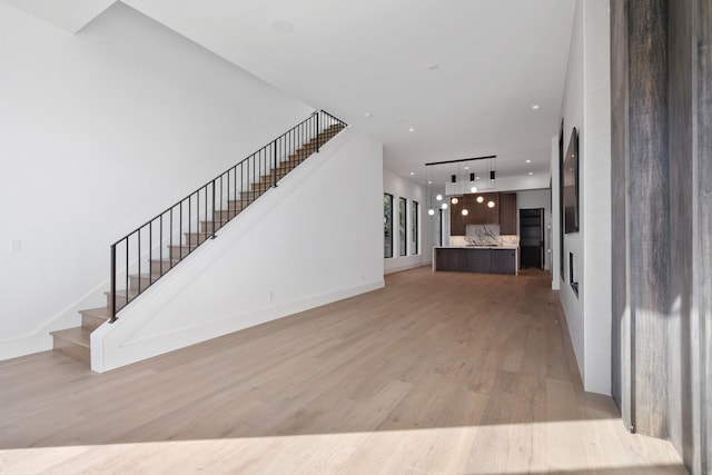 unfurnished living room with light wood-type flooring, recessed lighting, stairs, and baseboards