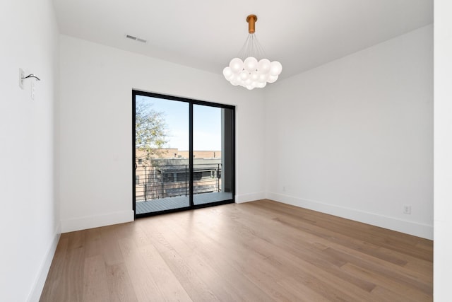 spare room featuring a notable chandelier, visible vents, baseboards, and light wood-type flooring