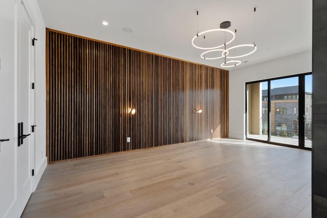empty room with light wood finished floors and a notable chandelier