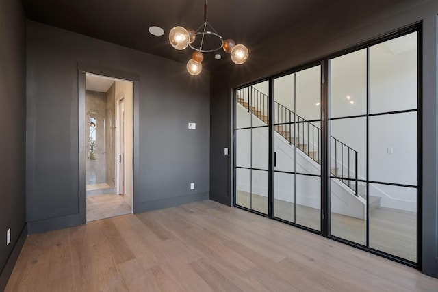 unfurnished room with baseboards, light wood-style flooring, and a notable chandelier