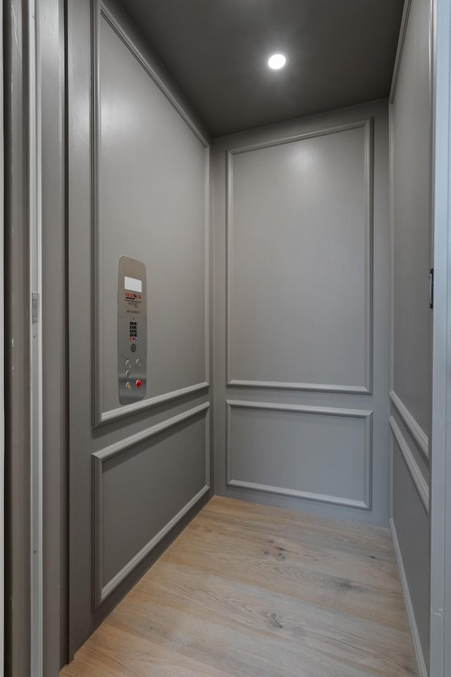 room details with recessed lighting, a decorative wall, elevator, and wood finished floors
