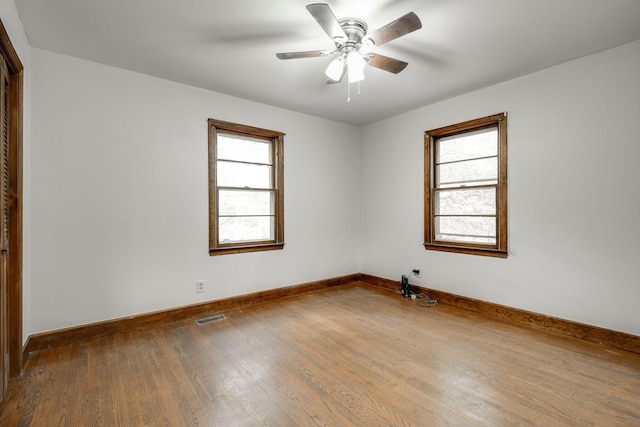 empty room with visible vents, a ceiling fan, baseboards, and wood finished floors