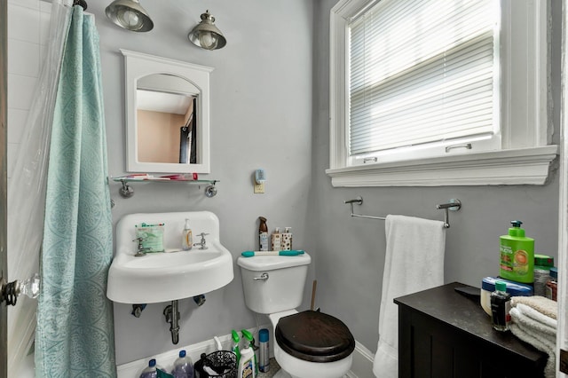 bathroom featuring a sink, toilet, baseboards, and a healthy amount of sunlight