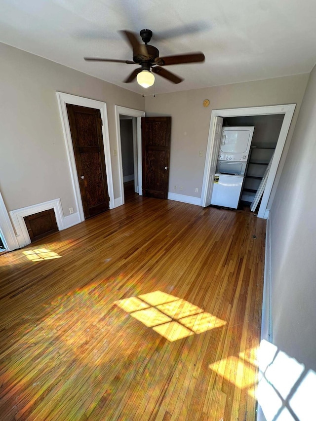unfurnished bedroom featuring baseboards, ceiling fan, hardwood / wood-style floors, a fireplace, and stacked washer / drying machine