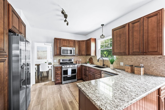 kitchen with light stone countertops, a sink, a peninsula, light wood finished floors, and stainless steel appliances