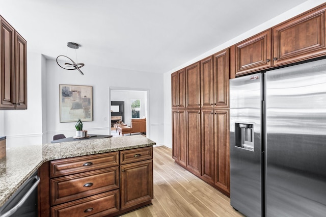 kitchen featuring stainless steel appliances, light stone countertops, light wood-style flooring, and a peninsula