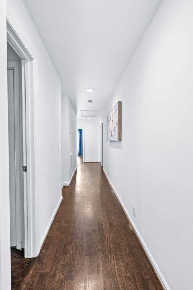 hall with dark wood-type flooring, attic access, and baseboards