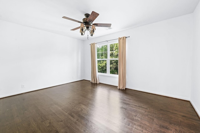 spare room with visible vents, a ceiling fan, dark wood finished floors, and baseboards