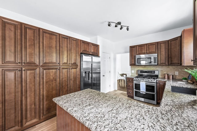 kitchen featuring backsplash, appliances with stainless steel finishes, light stone countertops, a peninsula, and light wood-style floors