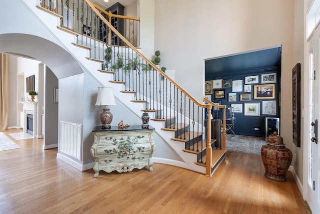 stairs with visible vents, wood finished floors, baseboards, a high ceiling, and arched walkways