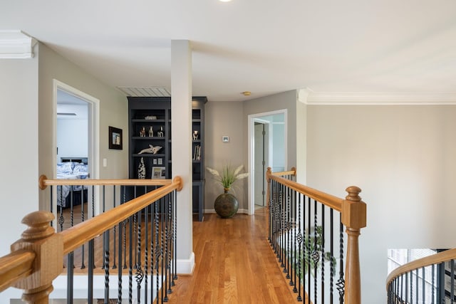 hall with crown molding, light wood finished floors, built in shelves, and an upstairs landing