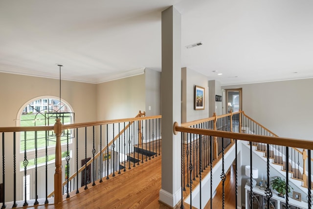 hall with crown molding, visible vents, wood finished floors, and an upstairs landing
