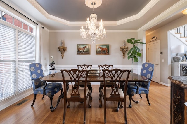 dining area featuring an inviting chandelier, a tray ceiling, light wood-style flooring, and visible vents