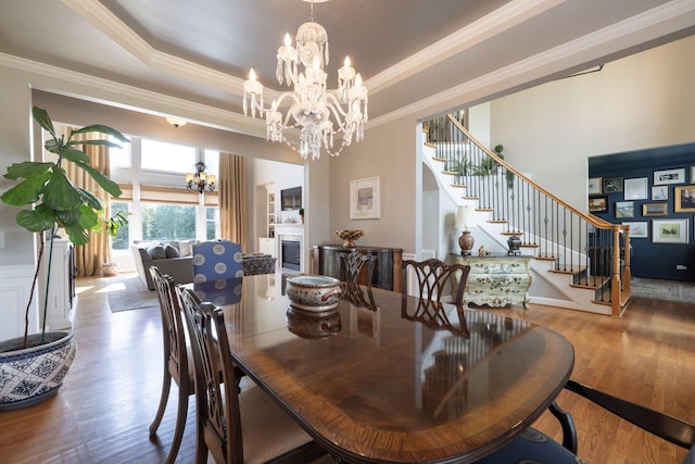 dining area with wood finished floors, a raised ceiling, an inviting chandelier, ornamental molding, and stairs