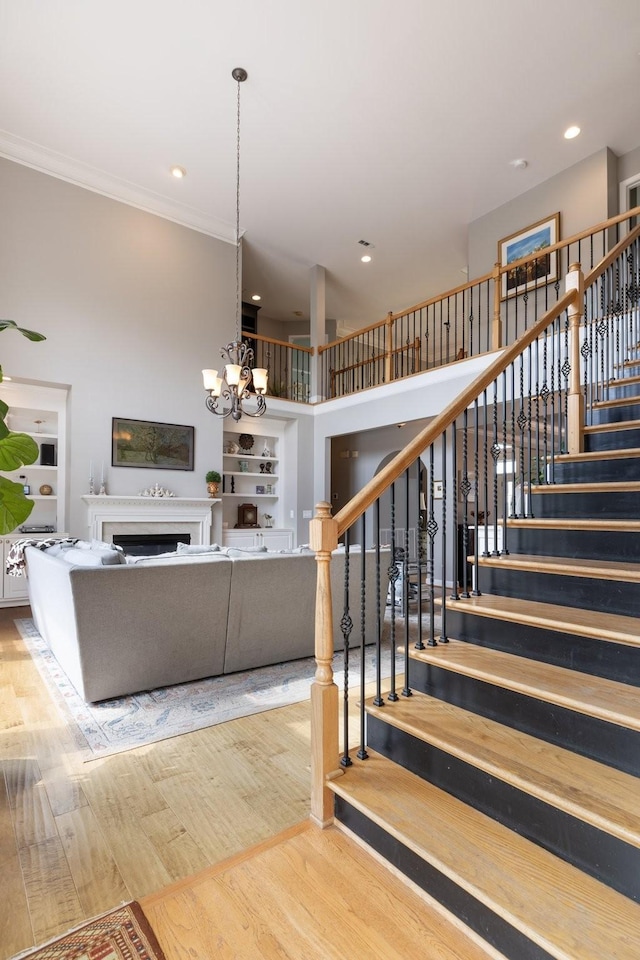 stairs featuring crown molding, a notable chandelier, a fireplace, recessed lighting, and wood finished floors