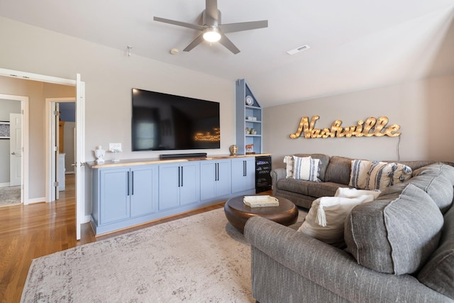 living room featuring built in features, a ceiling fan, vaulted ceiling, light wood-type flooring, and visible vents