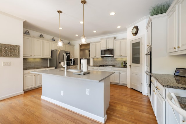 kitchen with an island with sink, a sink, appliances with stainless steel finishes, and backsplash