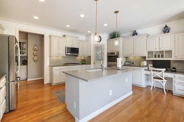 kitchen with ornamental molding, a kitchen island with sink, tasteful backsplash, a sink, and appliances with stainless steel finishes