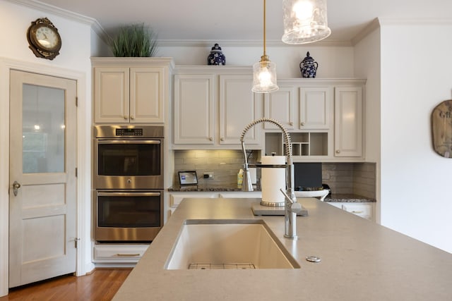 kitchen with a sink, double oven, ornamental molding, tasteful backsplash, and pendant lighting