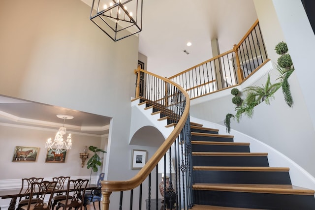 stairway with an inviting chandelier, a high ceiling, ornamental molding, and visible vents