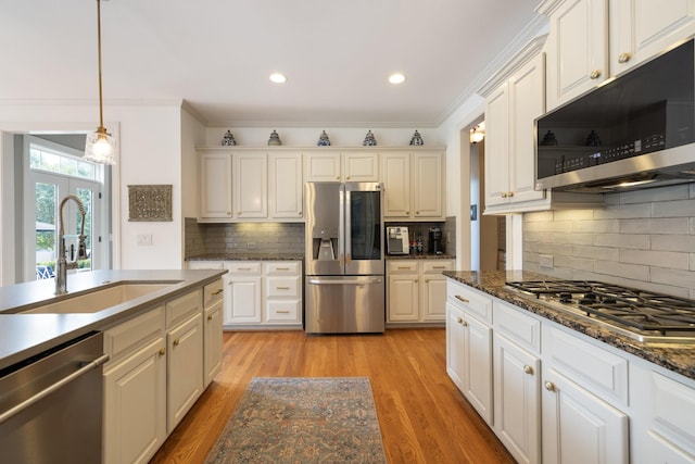 kitchen featuring backsplash, crown molding, appliances with stainless steel finishes, a sink, and light wood finished floors