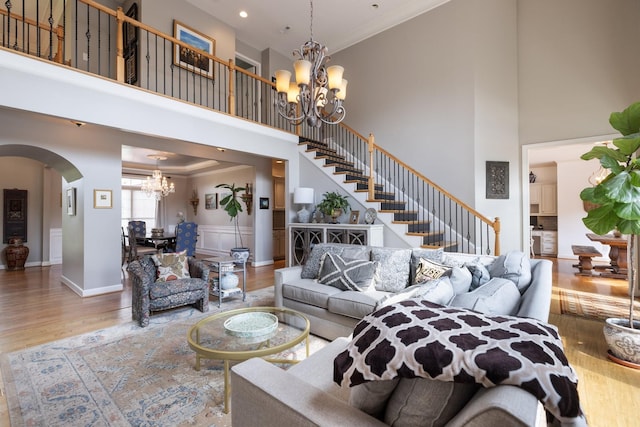 living area with arched walkways, wood finished floors, an inviting chandelier, a high ceiling, and stairs
