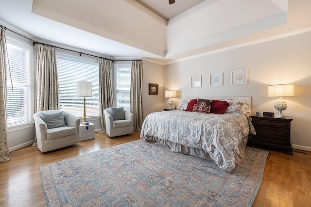 bedroom with baseboards, wood finished floors, and a raised ceiling