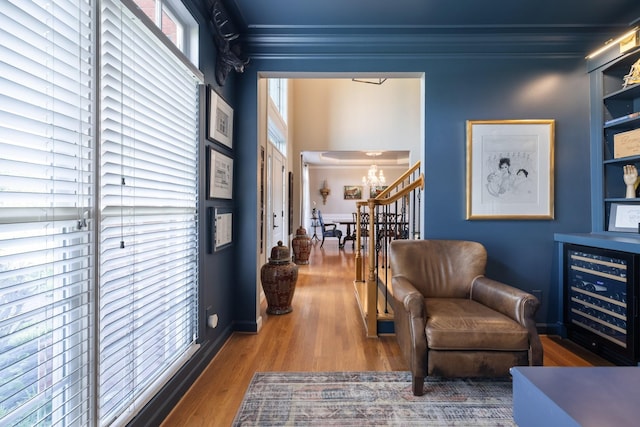living area with built in features, wood finished floors, a notable chandelier, wine cooler, and ornamental molding