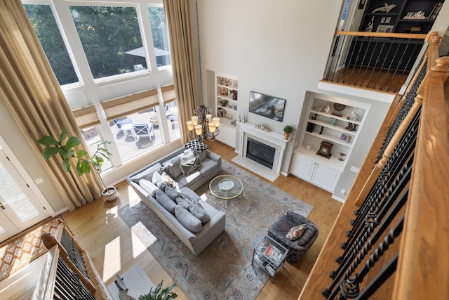 living area with wood finished floors, a fireplace with flush hearth, a high ceiling, and built in shelves