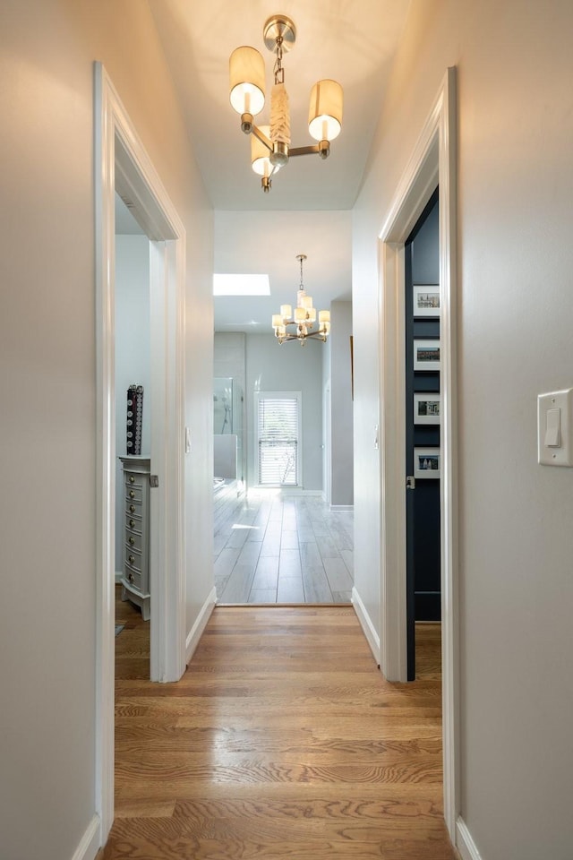 corridor with baseboards, a notable chandelier, and wood finished floors