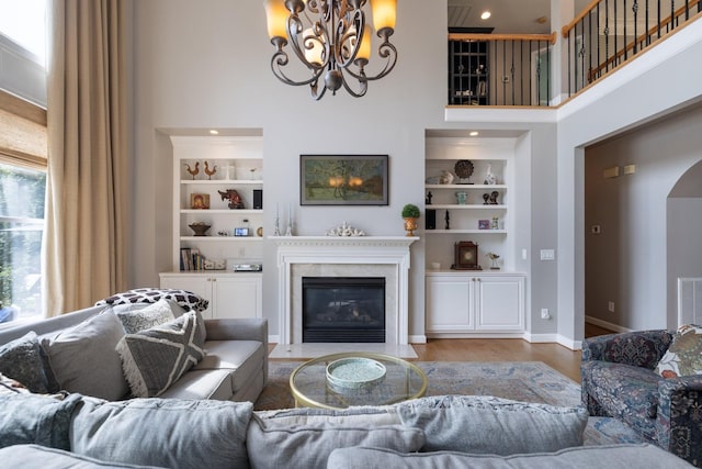 living area featuring a fireplace, arched walkways, a chandelier, built in features, and a towering ceiling