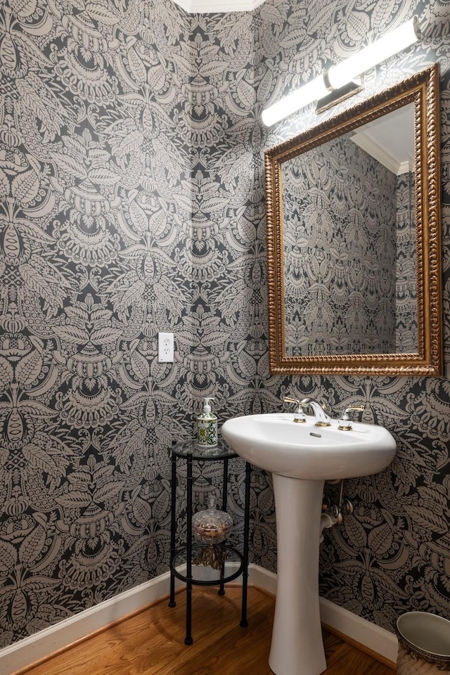 bathroom featuring baseboards, ornamental molding, wood finished floors, and wallpapered walls