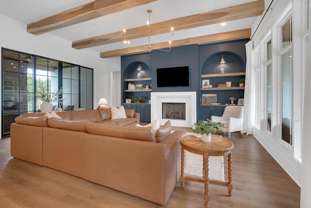 living area with wood finished floors, built in shelves, beam ceiling, and a fireplace