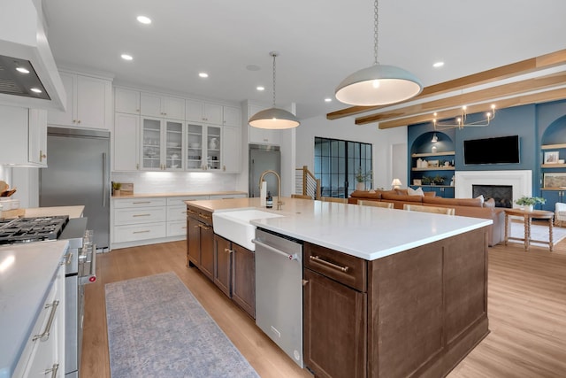 kitchen featuring a sink, light wood finished floors, wall chimney exhaust hood, white cabinetry, and high end appliances
