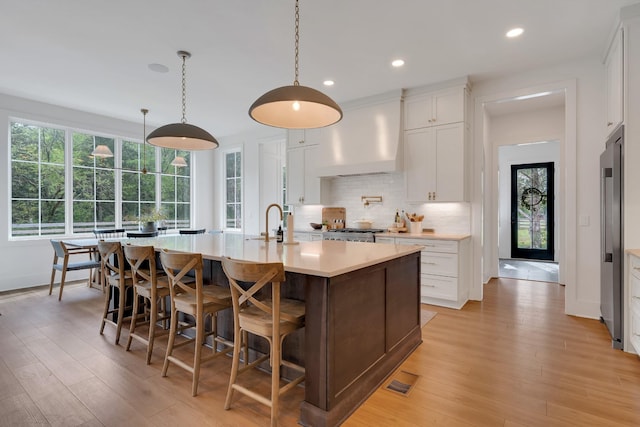kitchen with decorative backsplash, high end fridge, light wood-type flooring, light countertops, and wall chimney exhaust hood