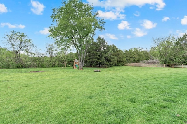 view of yard with a forest view, a rural view, fence, and a playground