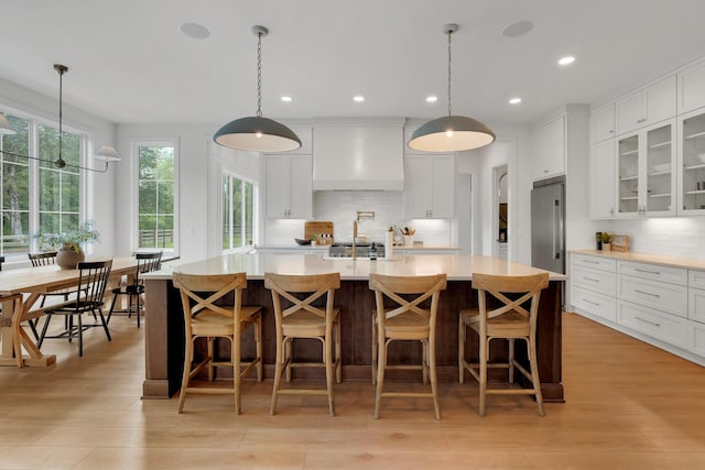kitchen with light countertops, white cabinetry, tasteful backsplash, custom exhaust hood, and glass insert cabinets