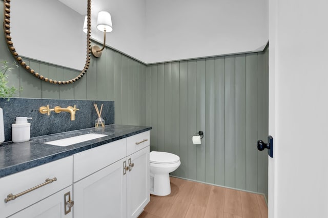 half bathroom featuring vanity, backsplash, toilet, and wood finished floors